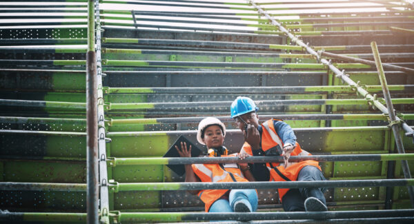 Tablet, man and woman on construction scaffolding with plan, collaboration and architecture. Digital app, discussion and contractor team on site for civil engineering, building or radio communication.