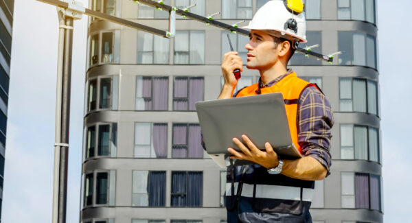 Contractor, Young man engineer checking information from laptop and commands with talking on radio call with colleague, Foreman working on building site and monitor antenna, urban development in city
